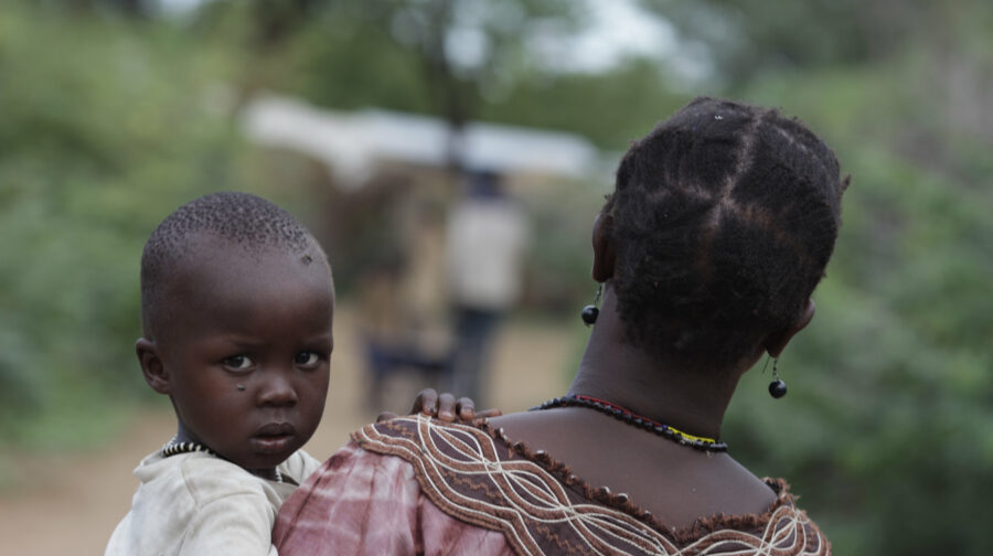 Sudanesische Frau trägt ihr kleines Kind auf dem Arm, das in die Kamera blickt.